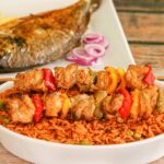 Close-up of flavorful Nigerian jollof rice with grilled chicken skewers and roasted fish.