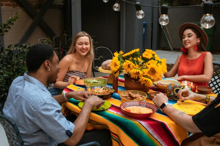 A group of friends enjoy a colorful meal outdoors with a sunflower centerpiece.